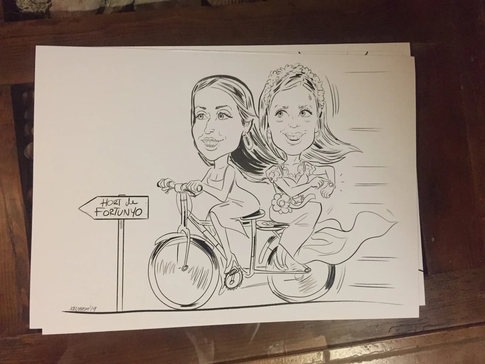 Caricatura en directe de la núvia i una amiga damunt d’una bicicleta