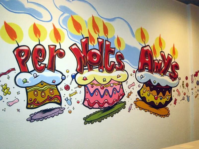 Mural pintat a la paret d’un local amb tres pastissos d’aniversari i el lema «Per molts anys»